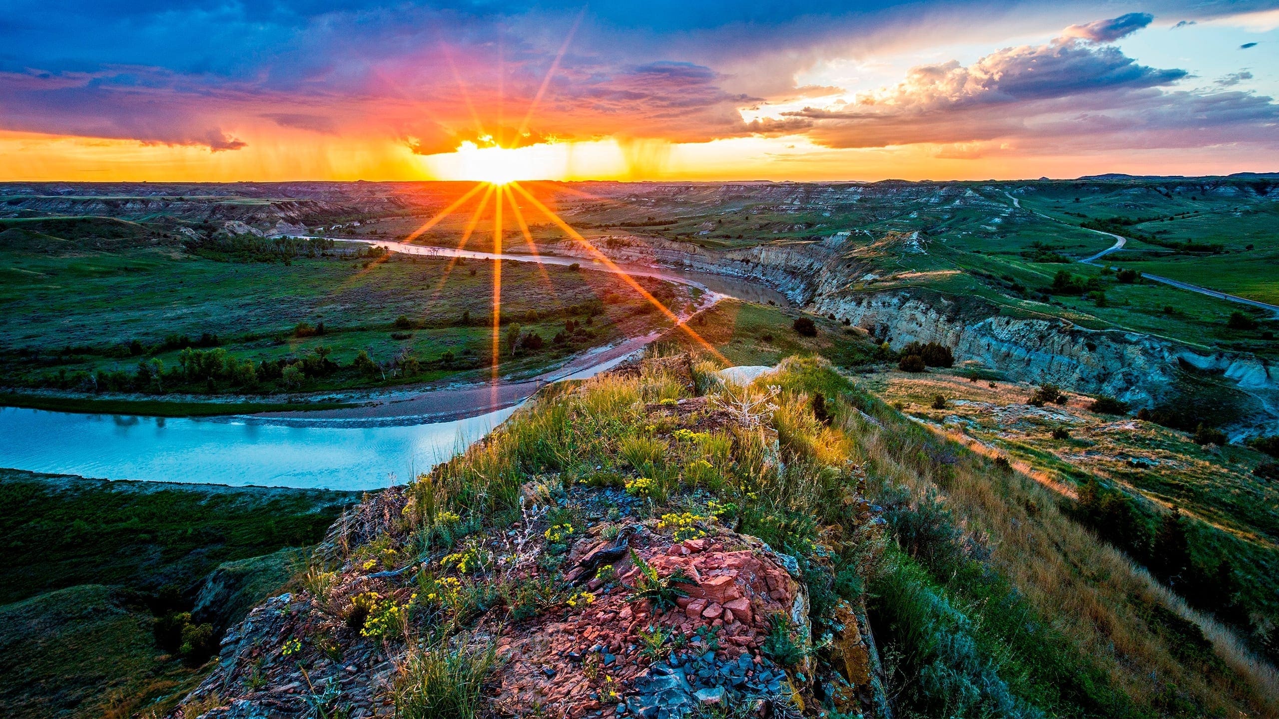 Rays from a setting sun burst through cloud to shine on a rocky butte and river down below.