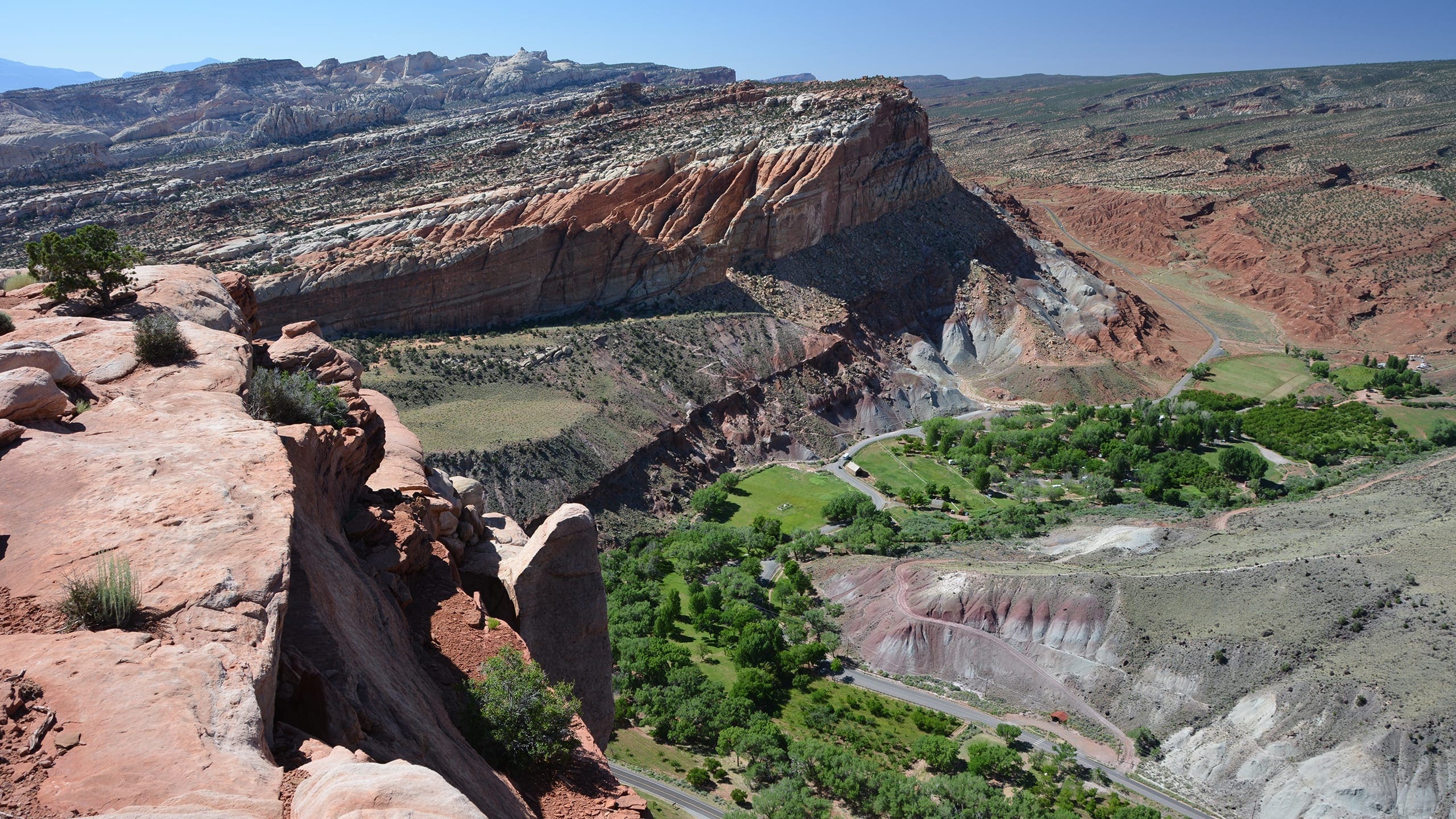 View from sandstone rim with a green valley, gray slopes, and red cliffs and blue sky.