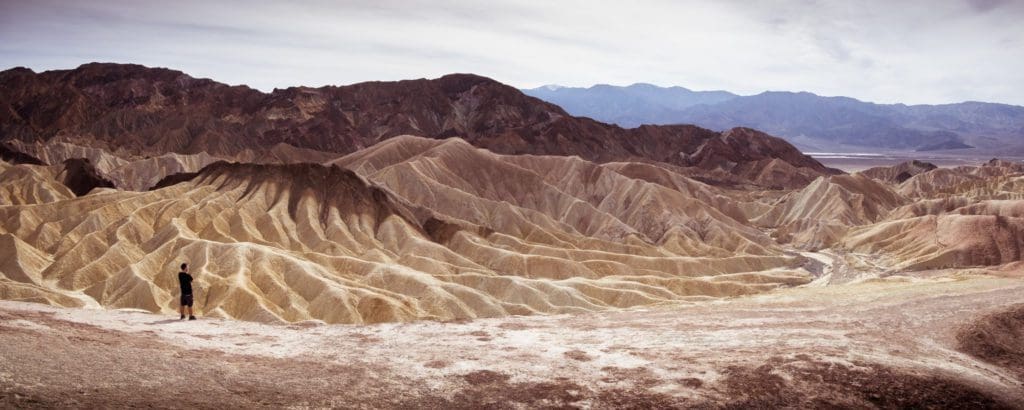 March 2021 - Park of the Month 13 A man standing below the massive cliffs near Zabriskie Point