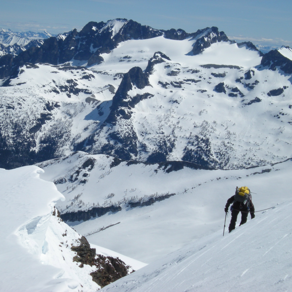 Climber on slope with mountain peaks in a background.